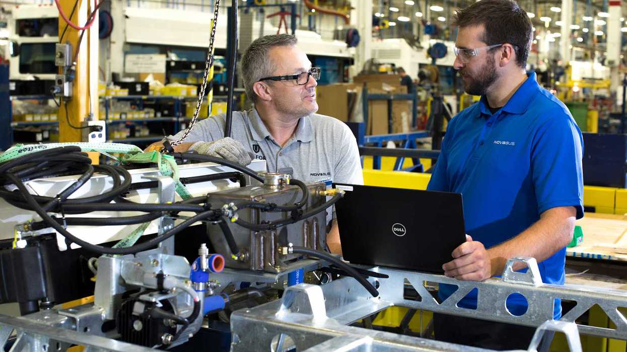 Deux employés de Nova Bus travaillent avec un ordinateur portable sur les composantes d’un véhicule en usine.