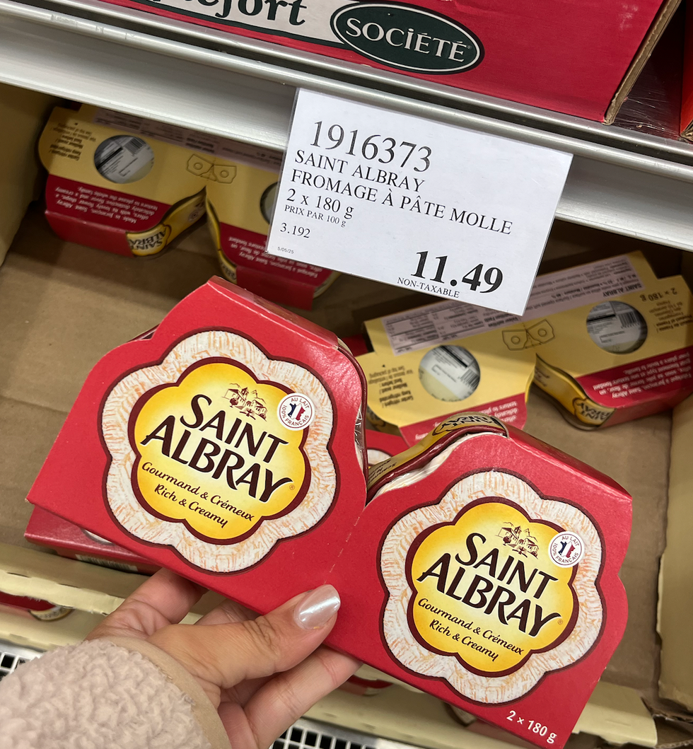 Deux fromages Saint Albray \u00e0 p\u00e2te molle dans une main au Costco.