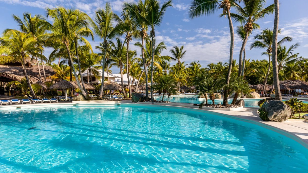 Deux grandes piscines entourées de palmiers sur le site d'un complexe hôtelier.