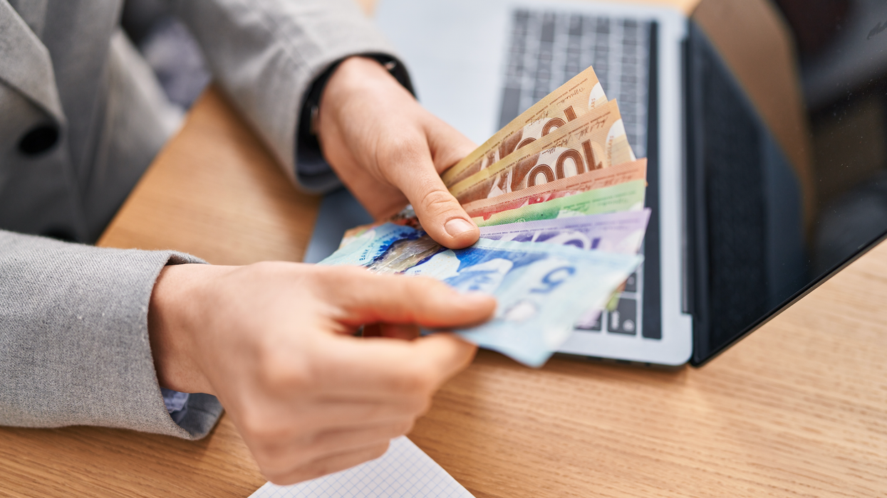 Deux mains tiennent des billets d'argent de 100 $, 50 $, 20 $, 10 $ et 5 $ devant un ordinateur portable.