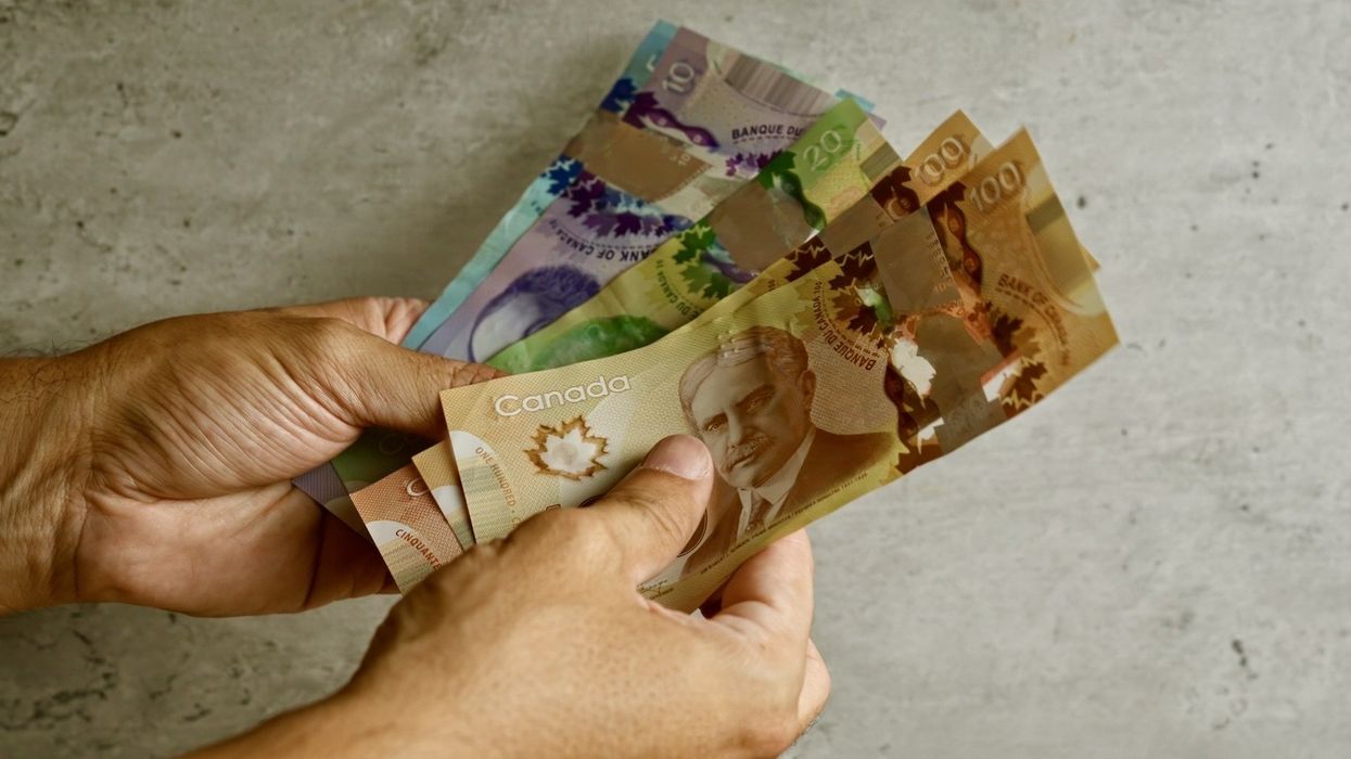 Deux mains tiennent des billets de 100 $, 20 $, 10 $ et 5 $ placés en éventail.