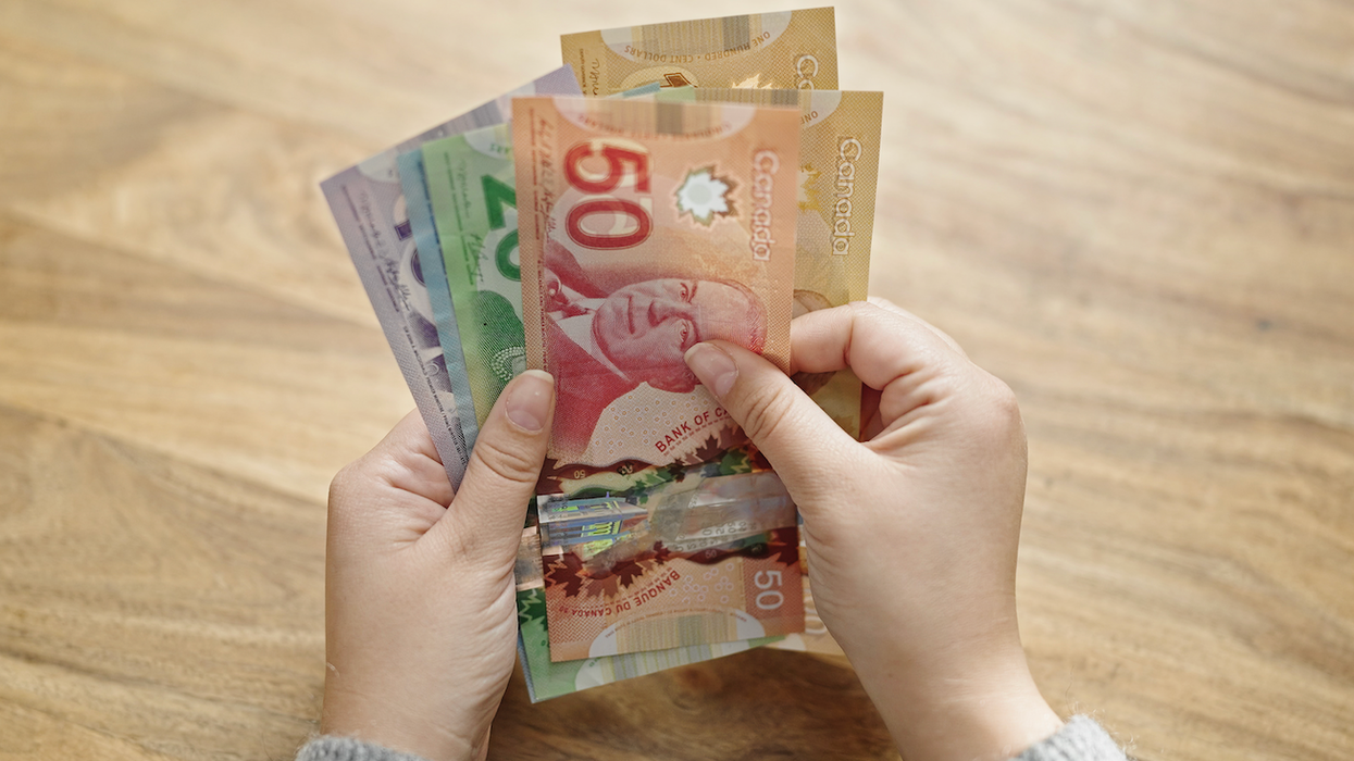Deux mains tiennent des billets de 100 $, 50 $, 20 $, 10 $ et 5 $.