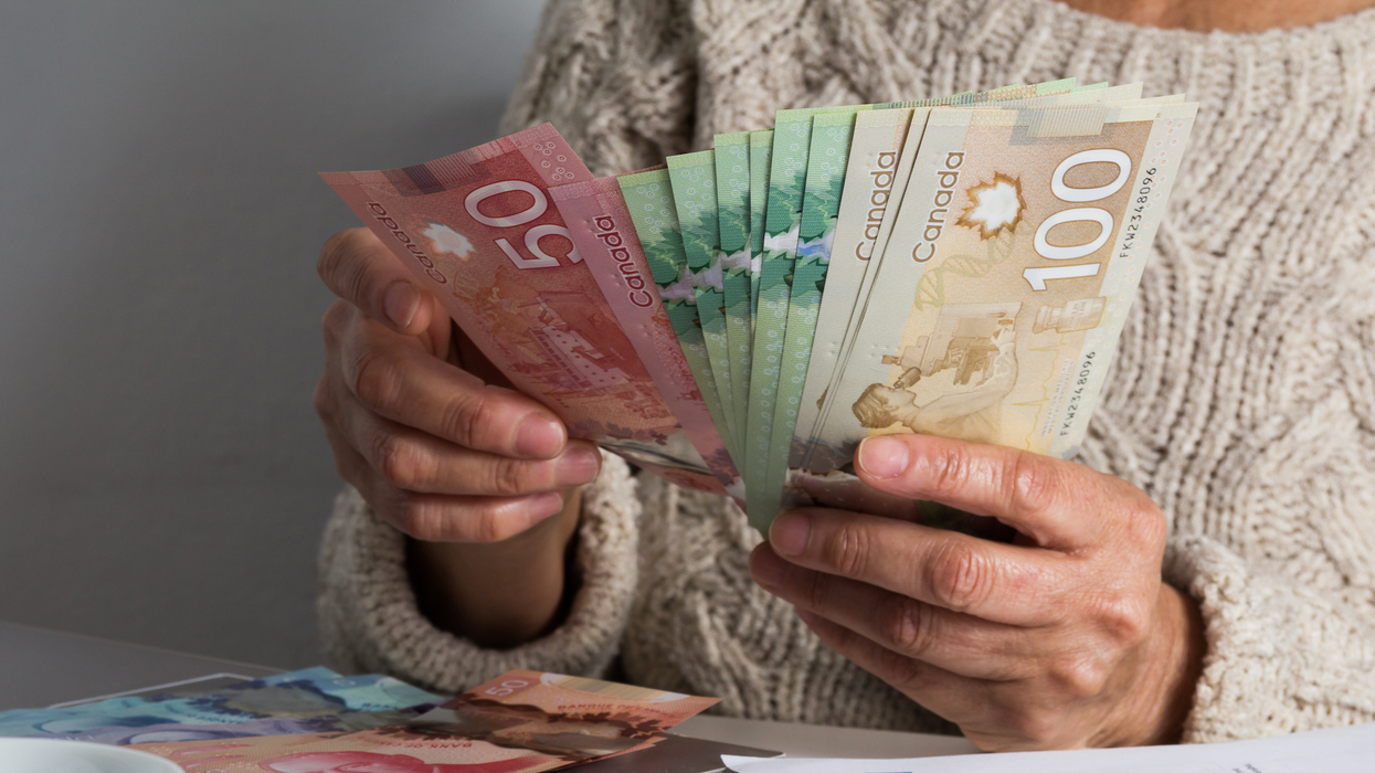 Deux mains tiennent des billets de 100 $, 50 $ et 20 $ devant une table où se trouvent des billets de 50 $ et 5 $.