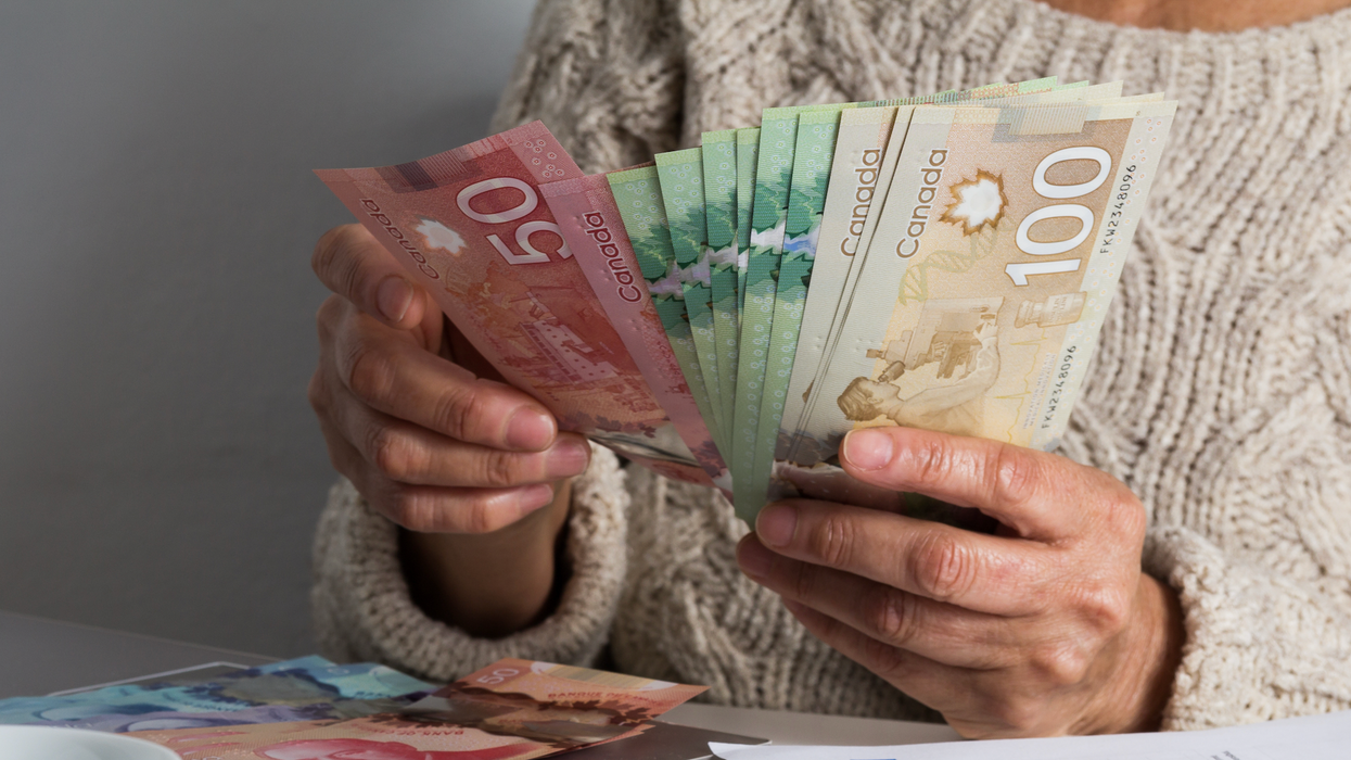 Deux mains tiennent des billets de 100 $, 50 $ et 20 $ devant une table où se trouvent des billets de 50 $ et 5 $.