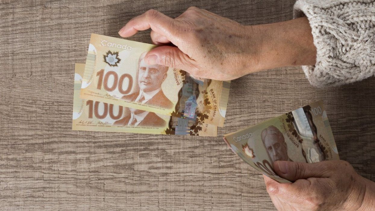 Deux mains tiennent des billets de 100 $ devant une table.