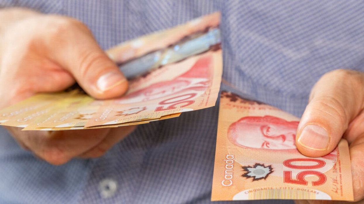Deux mains tiennent des billets de 50 $ canadien.