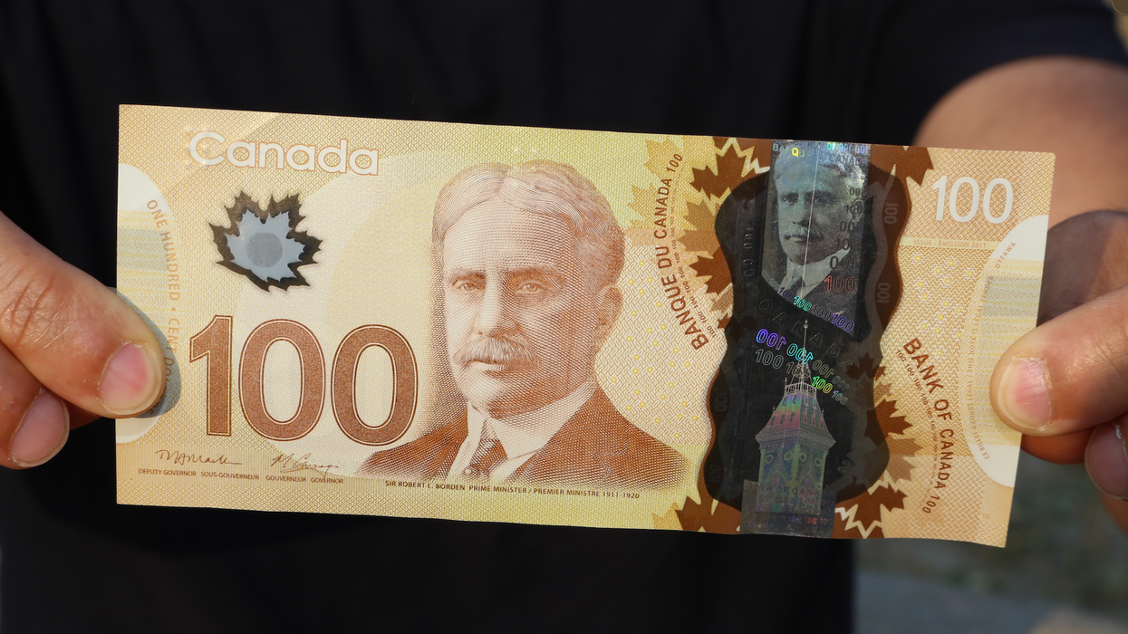 Deux mains tiennent un billet de 100 $.