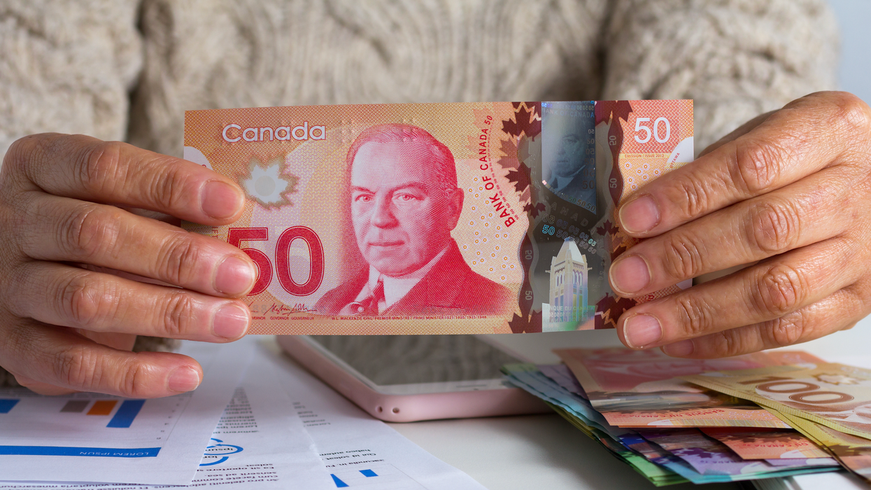 Deux mains tiennent un billet de 50 $ devant des documents, un cellulaire et des billets d'argent empilés sur une table.