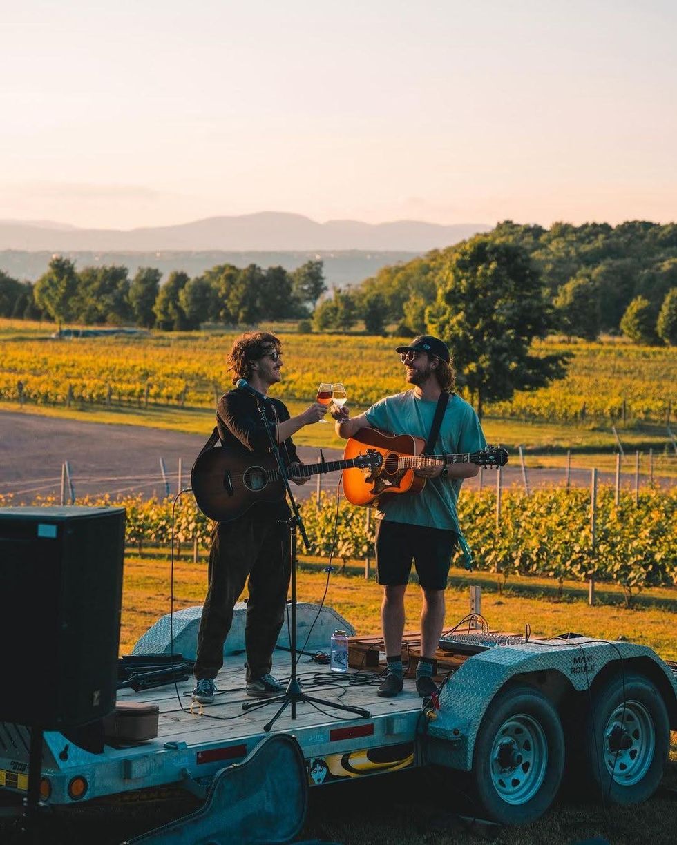 Deux musiciens trinquent avec leurs verres de vin lors d'une performance au Vignoble Sainte-P\u00e9tronille.