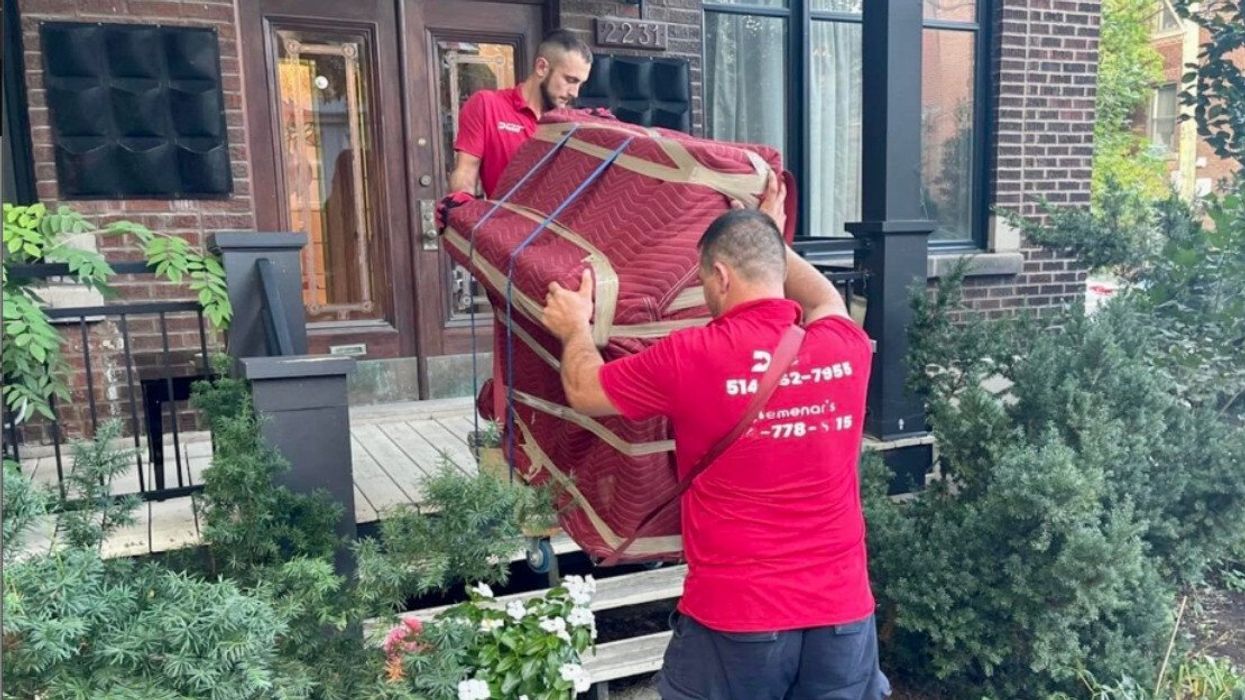 Deux personnes déménagent un meuble enveloppé dans une housse bourgogne.