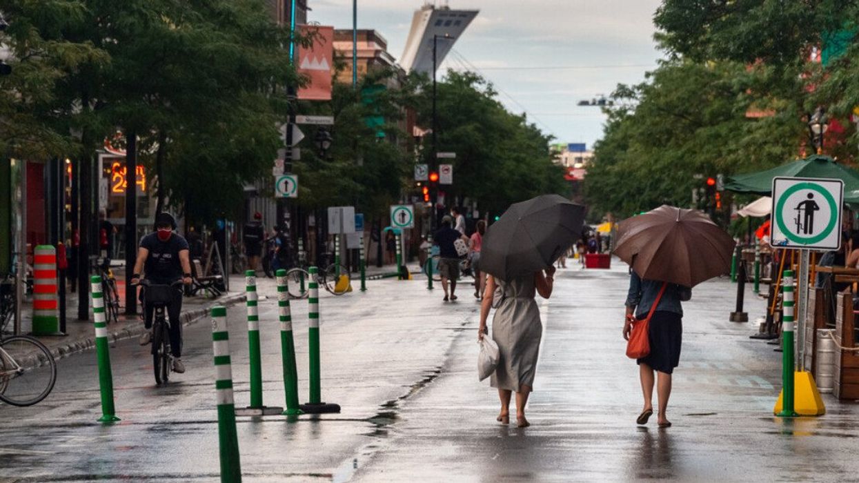Deux personnes marchent dans une rue piétonne à Montréal avec vue sur le Stade olympique.