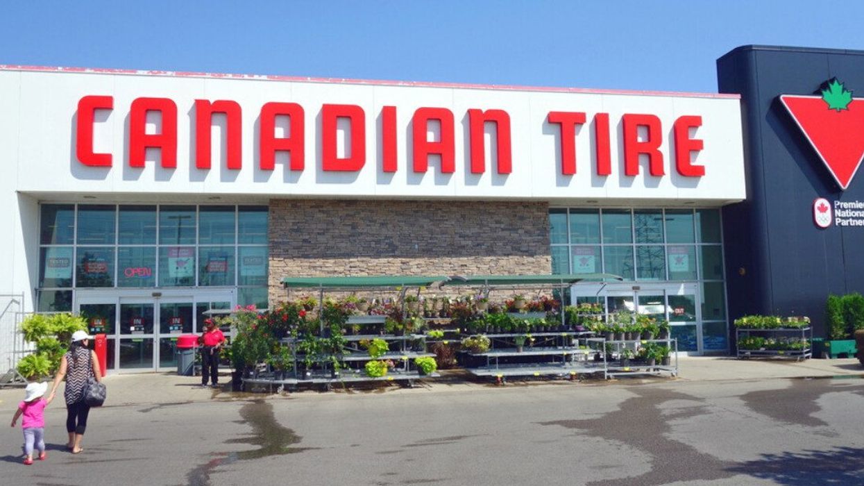 Deux personnes marchent en direction d'un Canadian Tire avec des fleurs installées devant la façade du magasin.