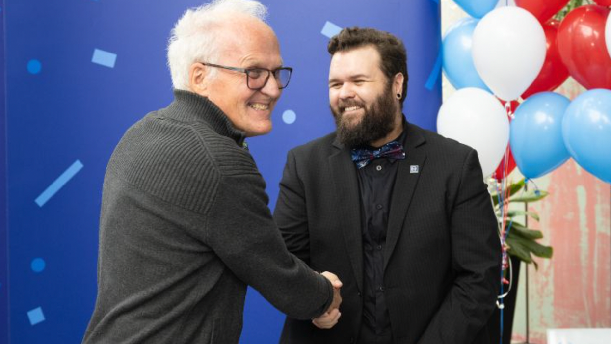 Deux personnes se serrent la main en souriant devant un fond bleu et des ballons.