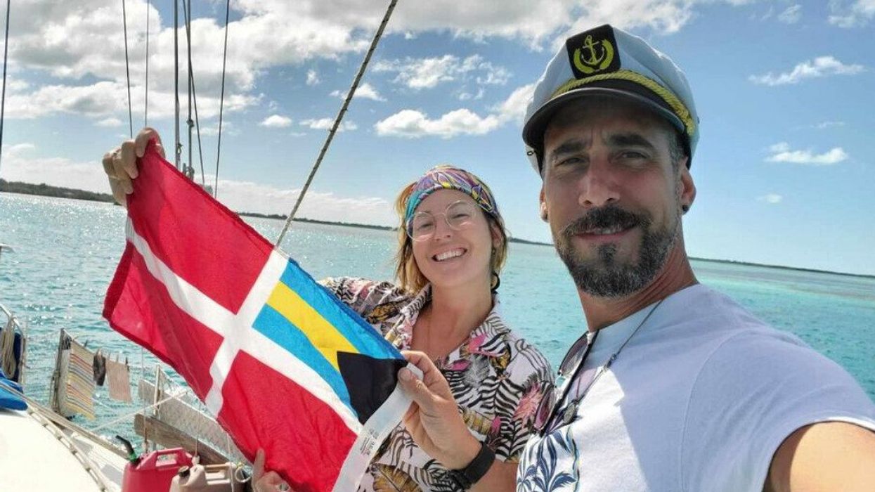 Deux personnes sont sur un voilier et l'une d'elles tient un drapeau de la marine marchande des Bahamas.