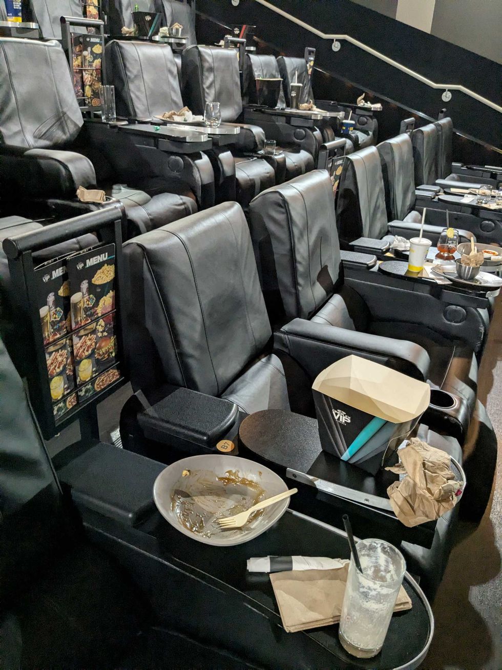 Dirty dishes and glasses sitting on top of movie theatre chairs