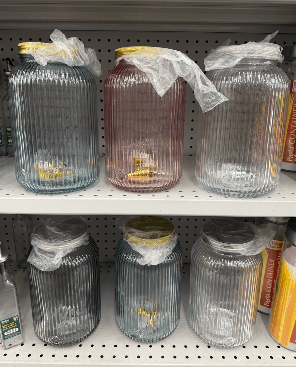 Distributeurs de boissons en verre stri\u00e9 rose, bleu et transparent avec couvercles et robinets, vendus 5 $ chez Dollarama.