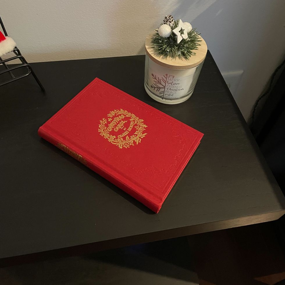 dollarama white holiday candle with pine branches, acorns and stars on the lid on a side table next to a red book