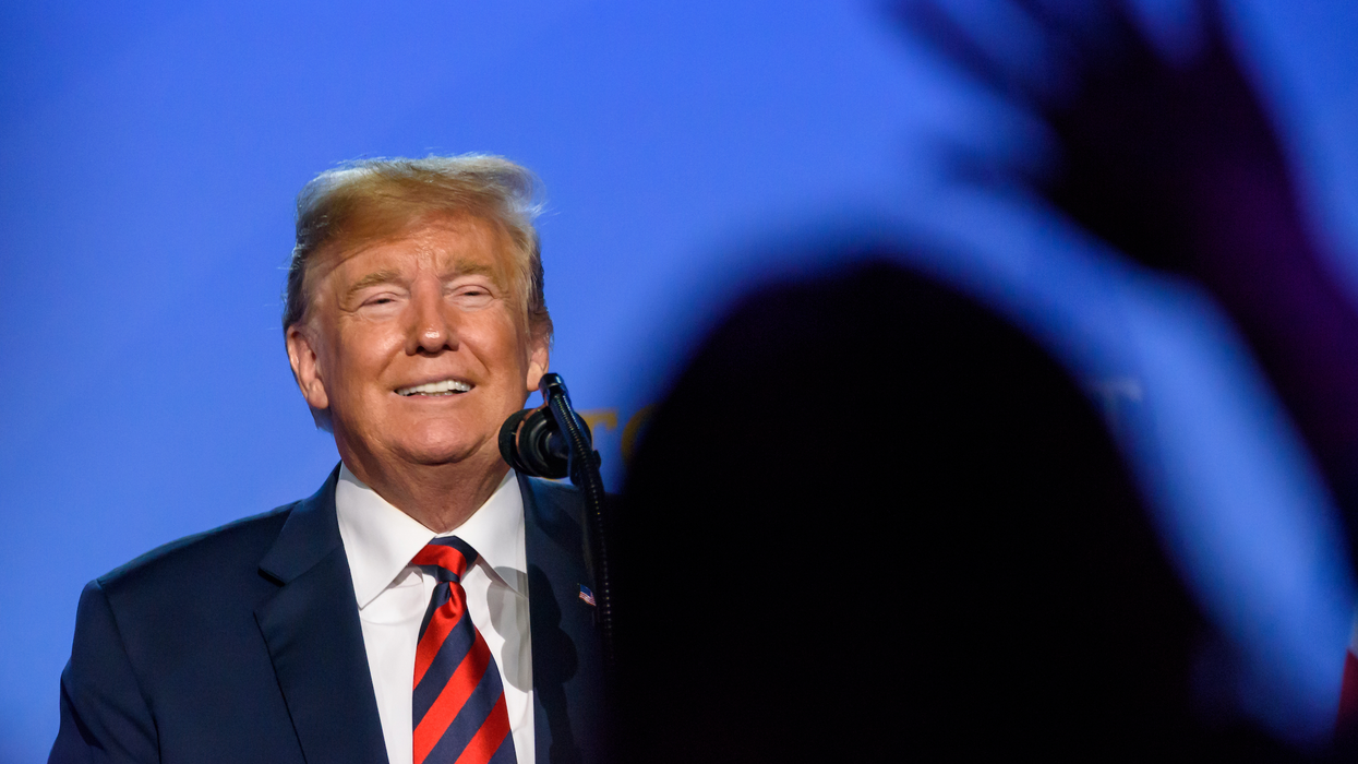 Donald Trum devant un micro et une fon bleu.