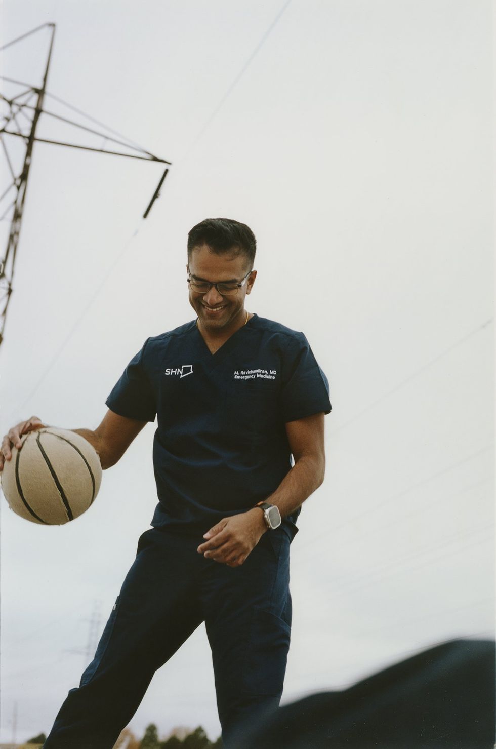 Dr. Mayoorendra Ravichandiran bounces a basketball and smiles while wearing his Scarborough Health Network scrubs.