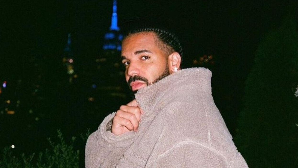 Drake holding the collar of his beige furry sweater.