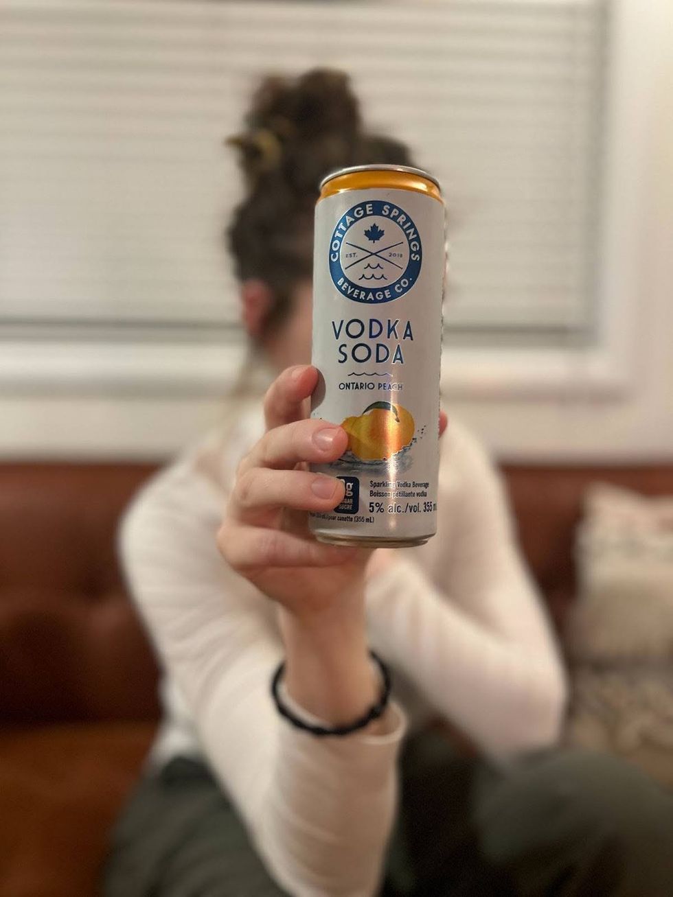 Elisha Barry holds a can of Cottage Springs Vodka Soda Ontario Peach up to the camera, obscuring her face.