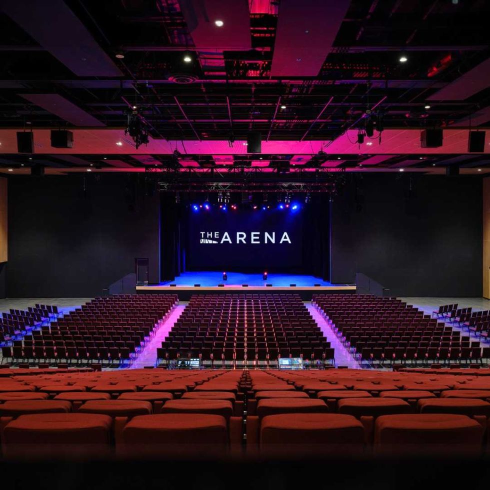 Empty seats in a 2,500-seat theatre. Above the empty stage, a sign says "The Arena."