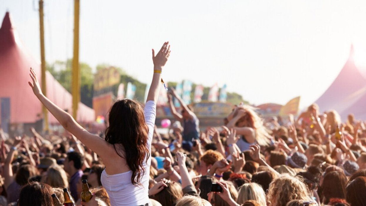 En avant-plan, une femme juchée sur les épaules d'une personne a les bras dans les airs au milieu de la foule d'un festival.