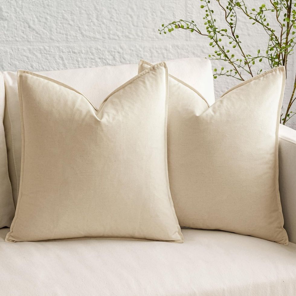 Ensemble de deux housses de coussin d\u00e9coratives en lin beige, d\u00e9montr\u00e9 sur un divan.