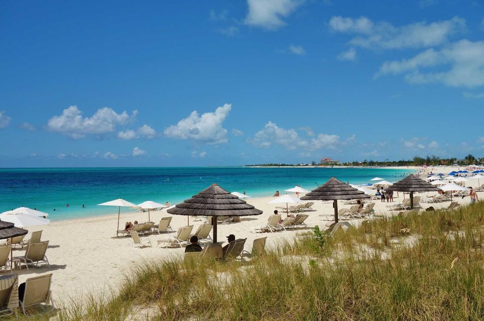 Fabric and grass beach umbrellas shading visitors to the white sands and blue water of Grace Bay, Turks and Caicos
