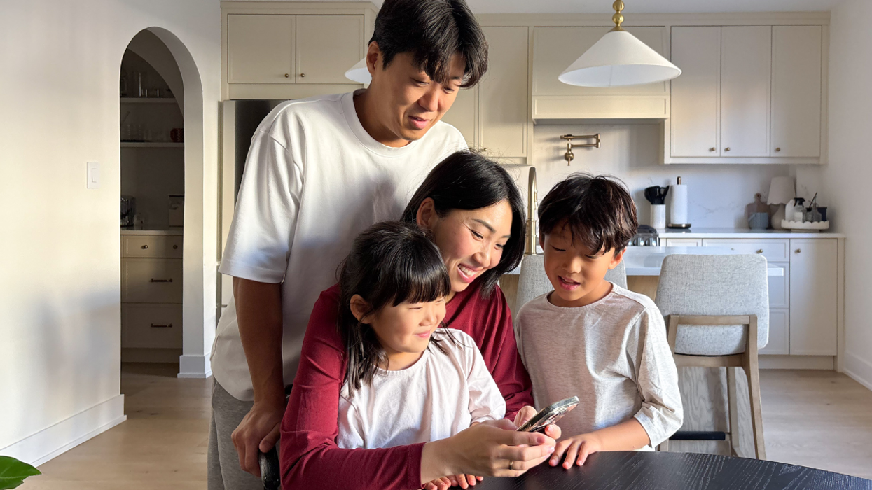 Famille de quatre personnes dans une cuisine moderne, souriant en regardant un téléphone ensemble.