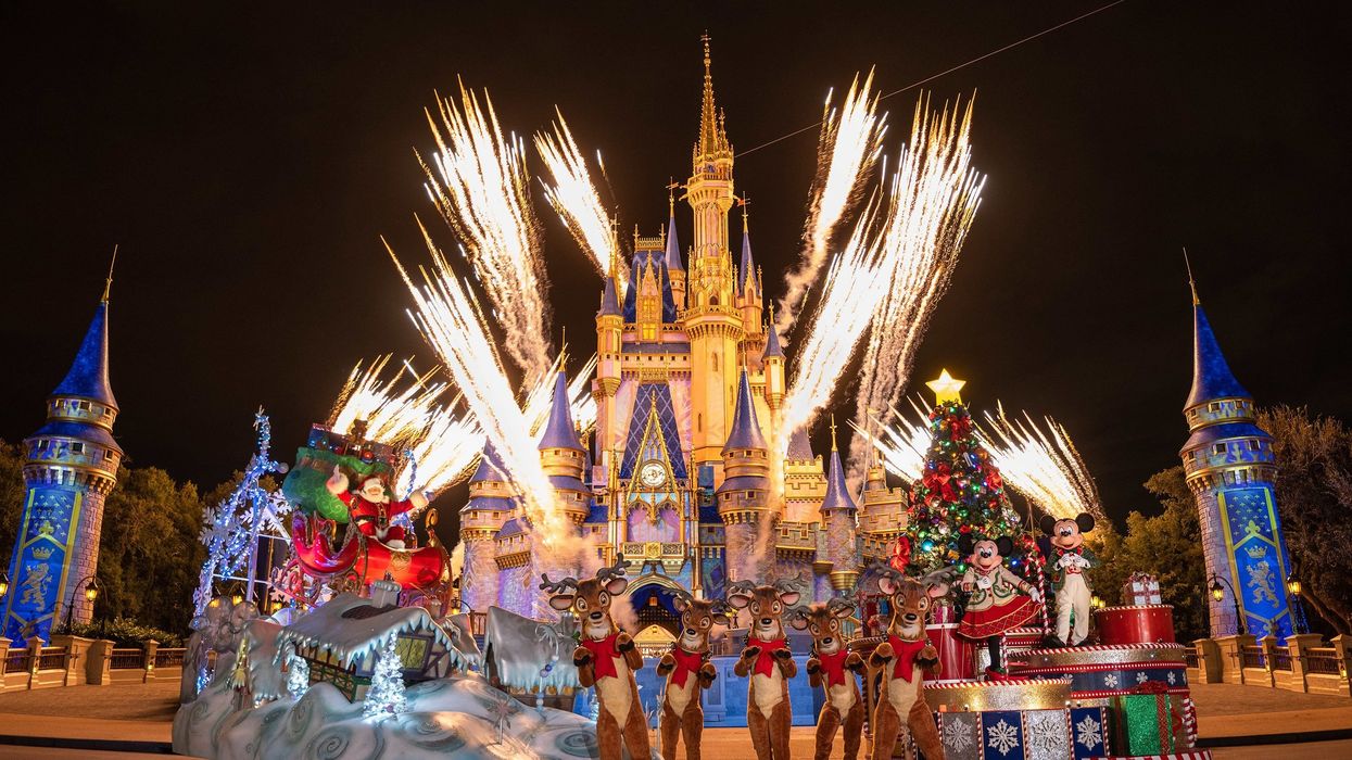 Fireworks burst above a brightly lit castle with Christmas decorations, featuring Santa in his sleigh, reindeer, and costumed characters like Mickey and Minnie Mouse.