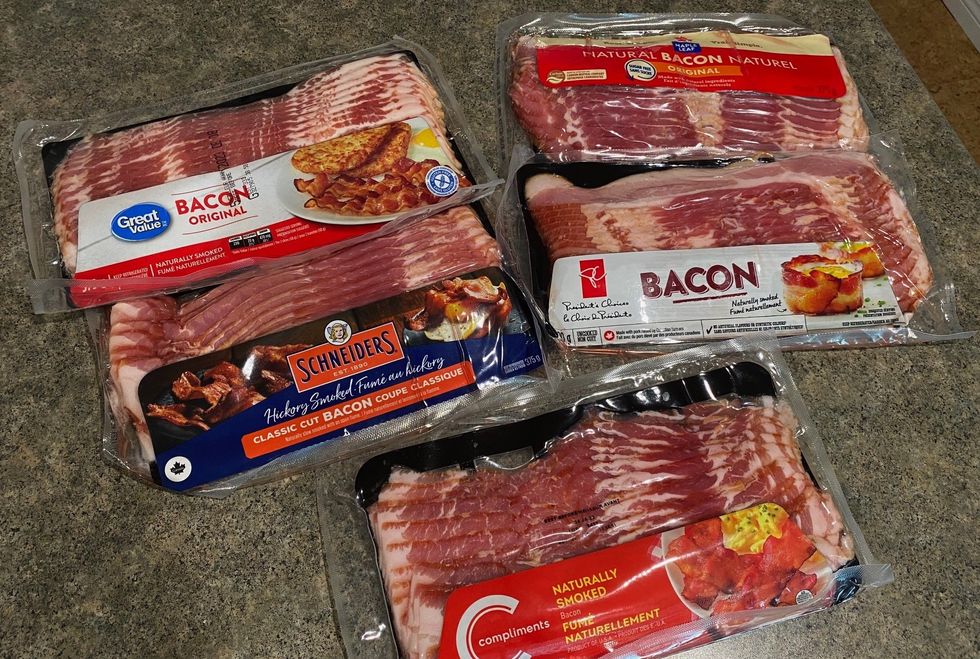 Five packages of bacon on a kitchen counter.