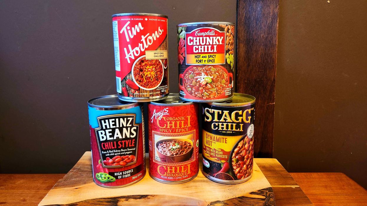 Five tins of chili stacked on each other against a wooden background and wooden table.