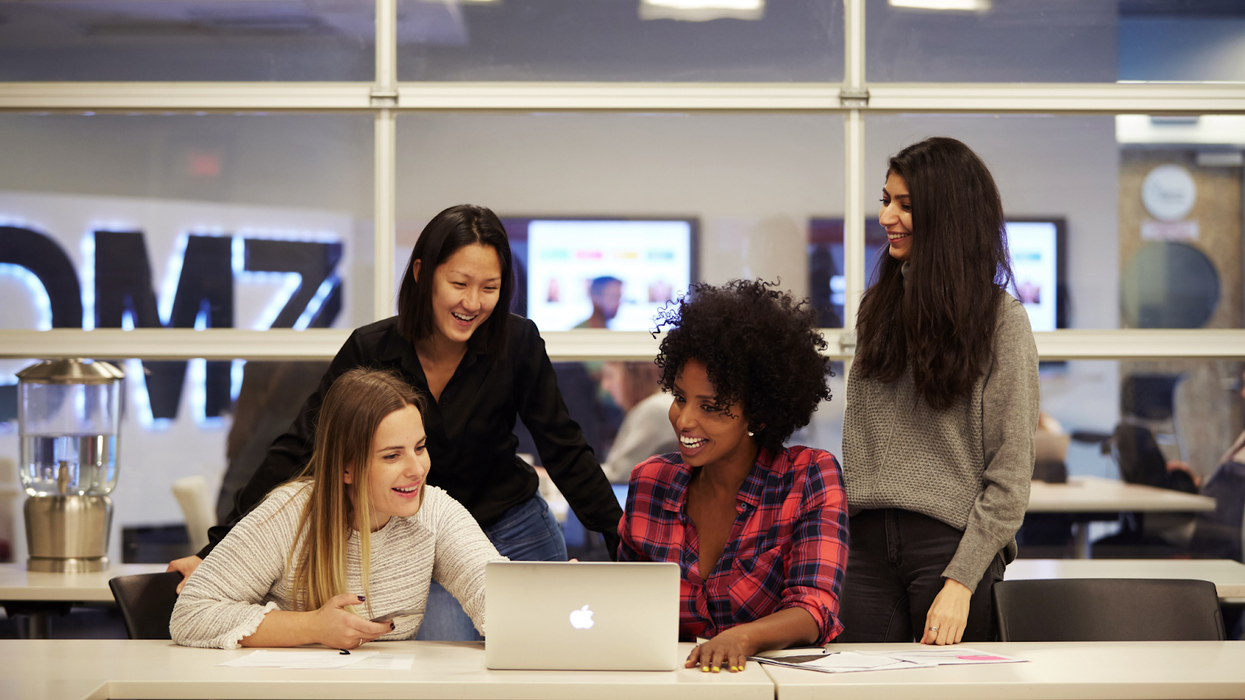 Four colleagues at DMZ Toronto looking at a laptop and smiling.