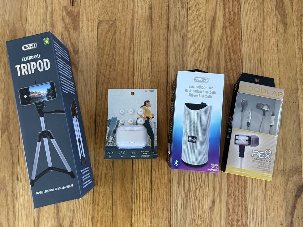 Four different items in boxes sitting on a floor, including a tripod, two sets of headphones and a Bluetooth speaker.