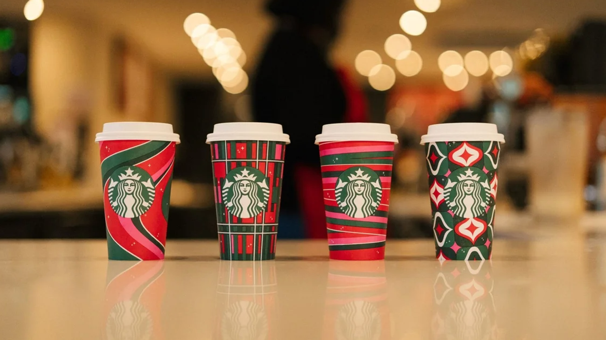 Four festive Starbucks holiday cups on a white counter.