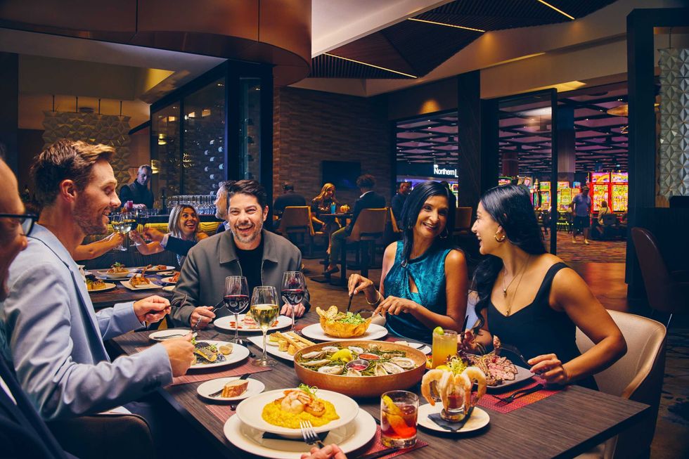 Four friends around a large table in a restaurant, laughing and smiling while drinking and eating.
