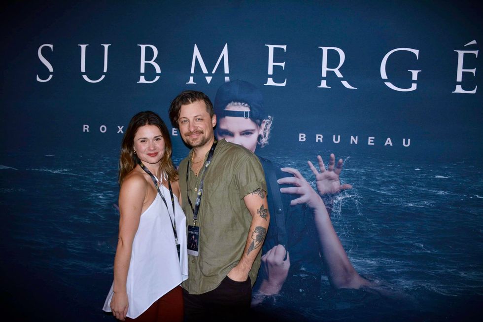 Fr\u00e9d\u00e9rique Dufort et J\u00e9r\u00f4me Couture qui posent devant l'affiche de Submerg\u00e9.