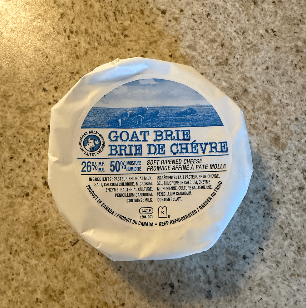 Fromage brie de ch\u00e8vre entier emball\u00e9 dans un papier blanc achet\u00e9 au Liquidation Marie et pos\u00e9 sur un comptoir.