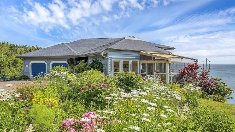 Front of the house for sale with a flower garden in front of it and the ocean behind it.