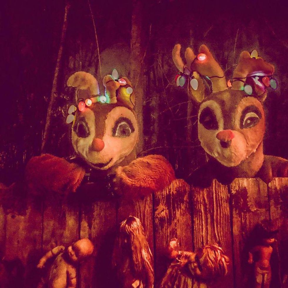 Giant reindeer looking over a fence with creepy dolls on it.