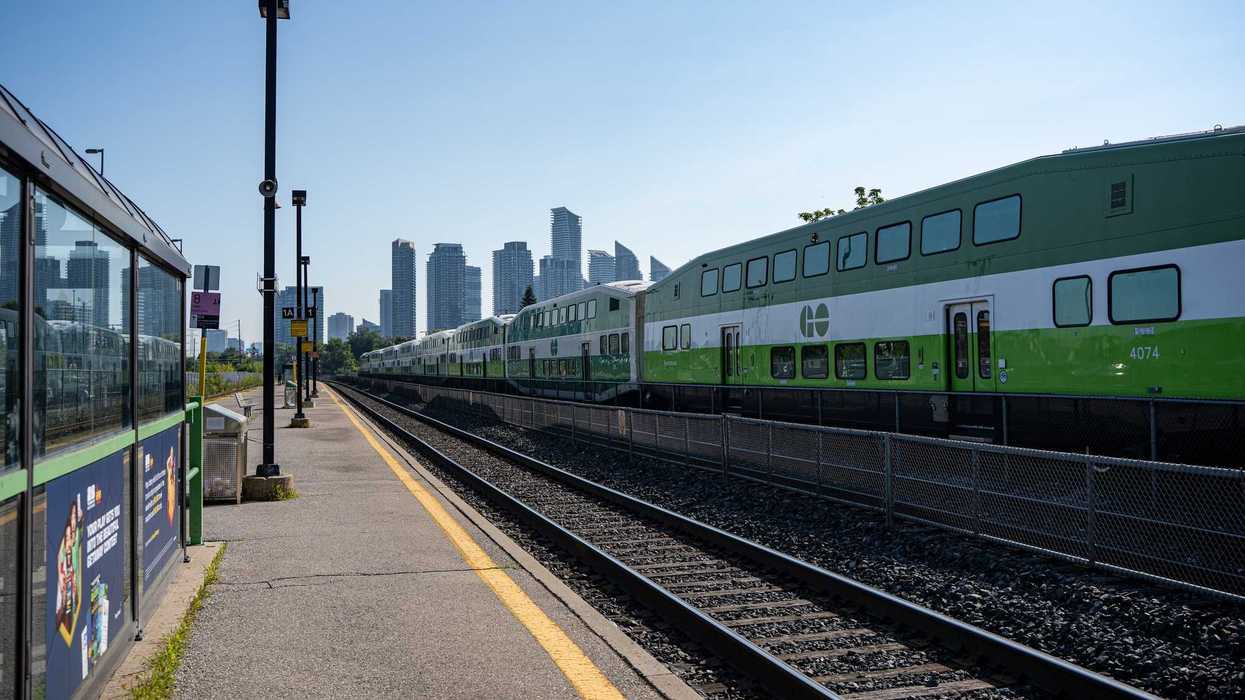 go train on tracks at go transit station in toronto with city skyline in background