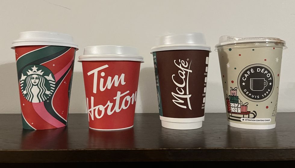Gobelet du Starbucks, du Tim Hortons, du McDonald's et du Caf\u00e9 D\u00e9p\u00f4t sur une tablette en bois.