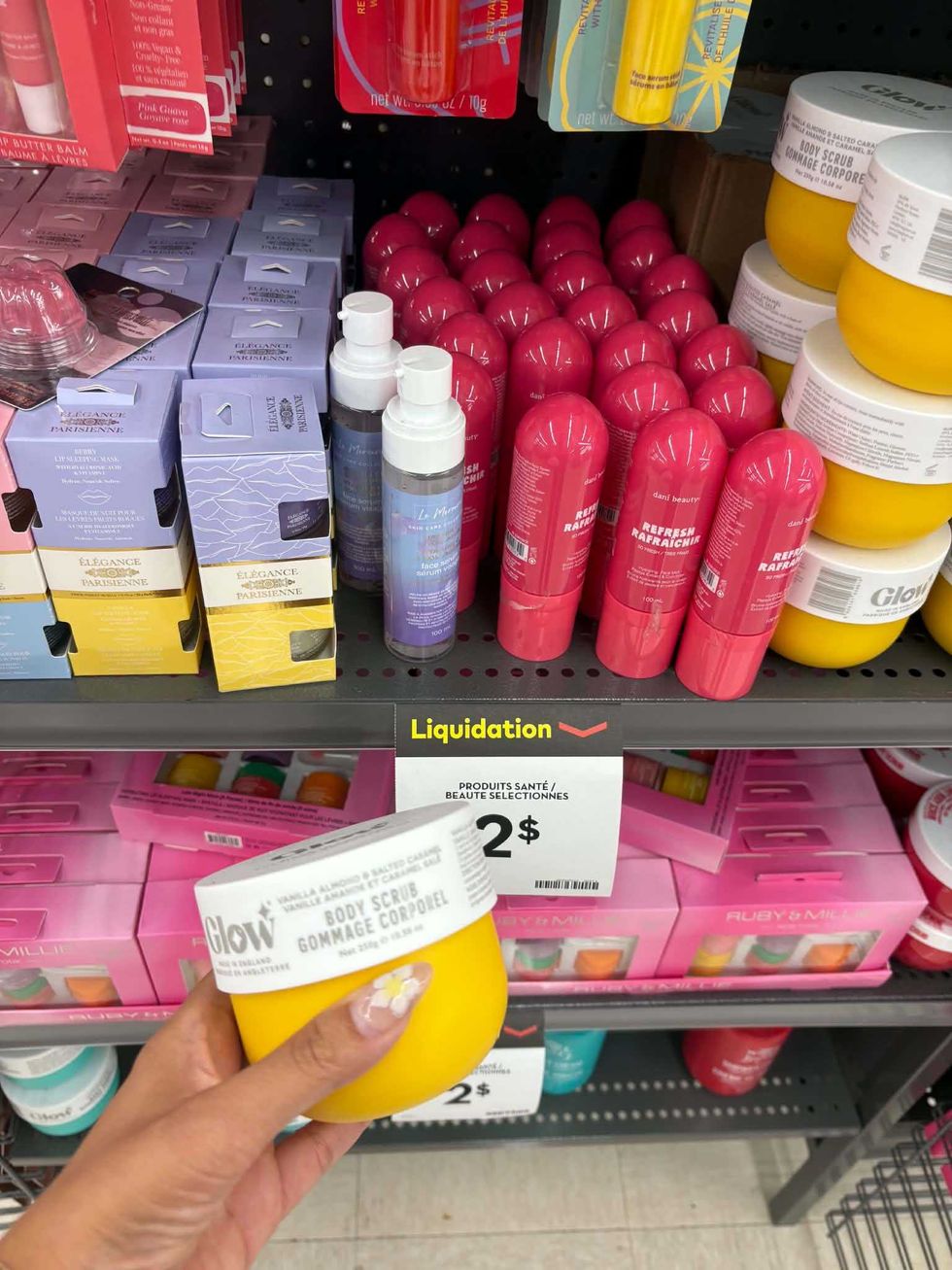 Gommage corporel Glow tenu devant une tablette de produits beaut\u00e9 affich\u00e9s \u00e0 2 $.
