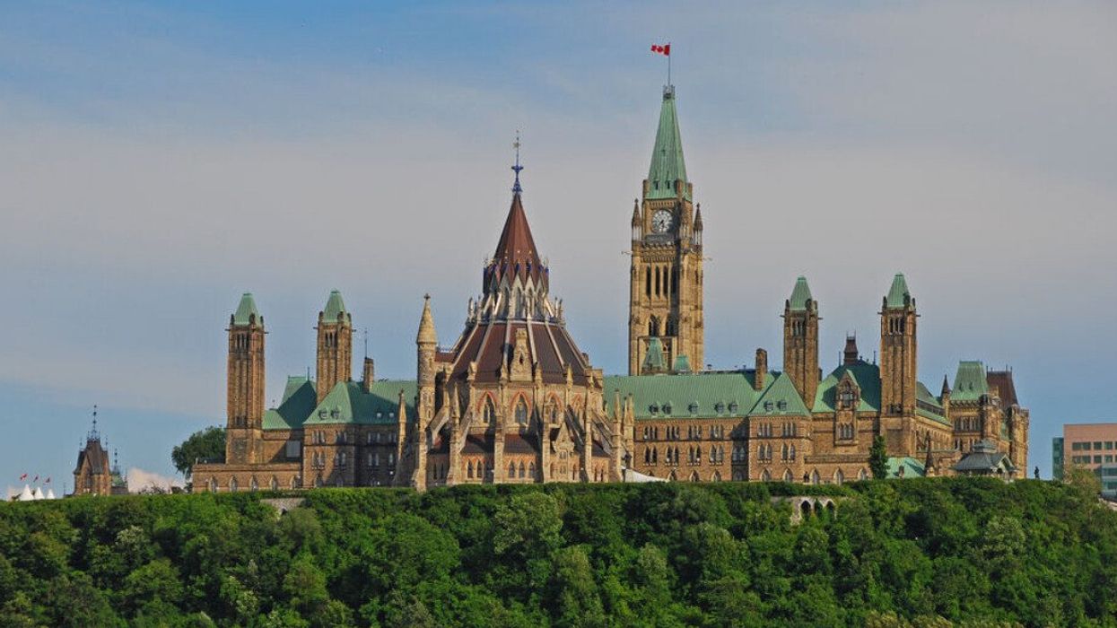 Gothic revival-style buildings set on a hill, including a clock tower with a Canadian flag at the top.