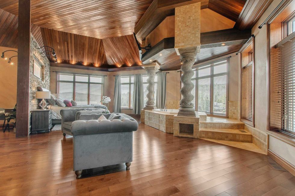 Grande chambre avec planchers en bois, colonnes sculpt\u00e9es et bain encastr\u00e9 pr\u00e8s des fen\u00eatres.