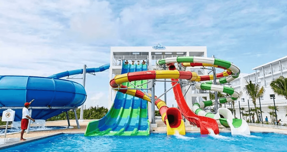 Grande piscine bord\u00e9e de palmiers avec espaces d\u00e9tente int\u00e9gr\u00e9s dans l\u2019eau au Riu Dunamar, en bord de mer \u00e0 Playa Mujeres.