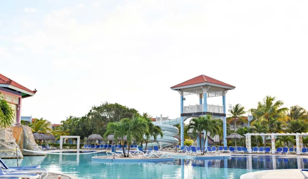 Grande piscine entour\u00e9e de palmiers et de chaises longues.
