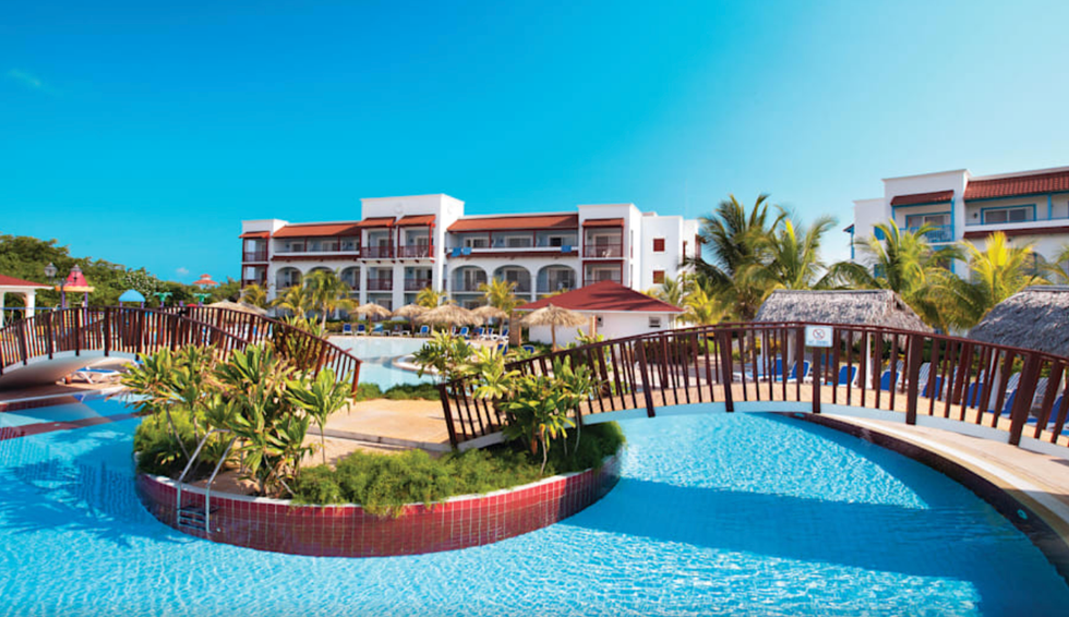 Grande piscine entour\u00e9e de palmiers et de chaises longues.