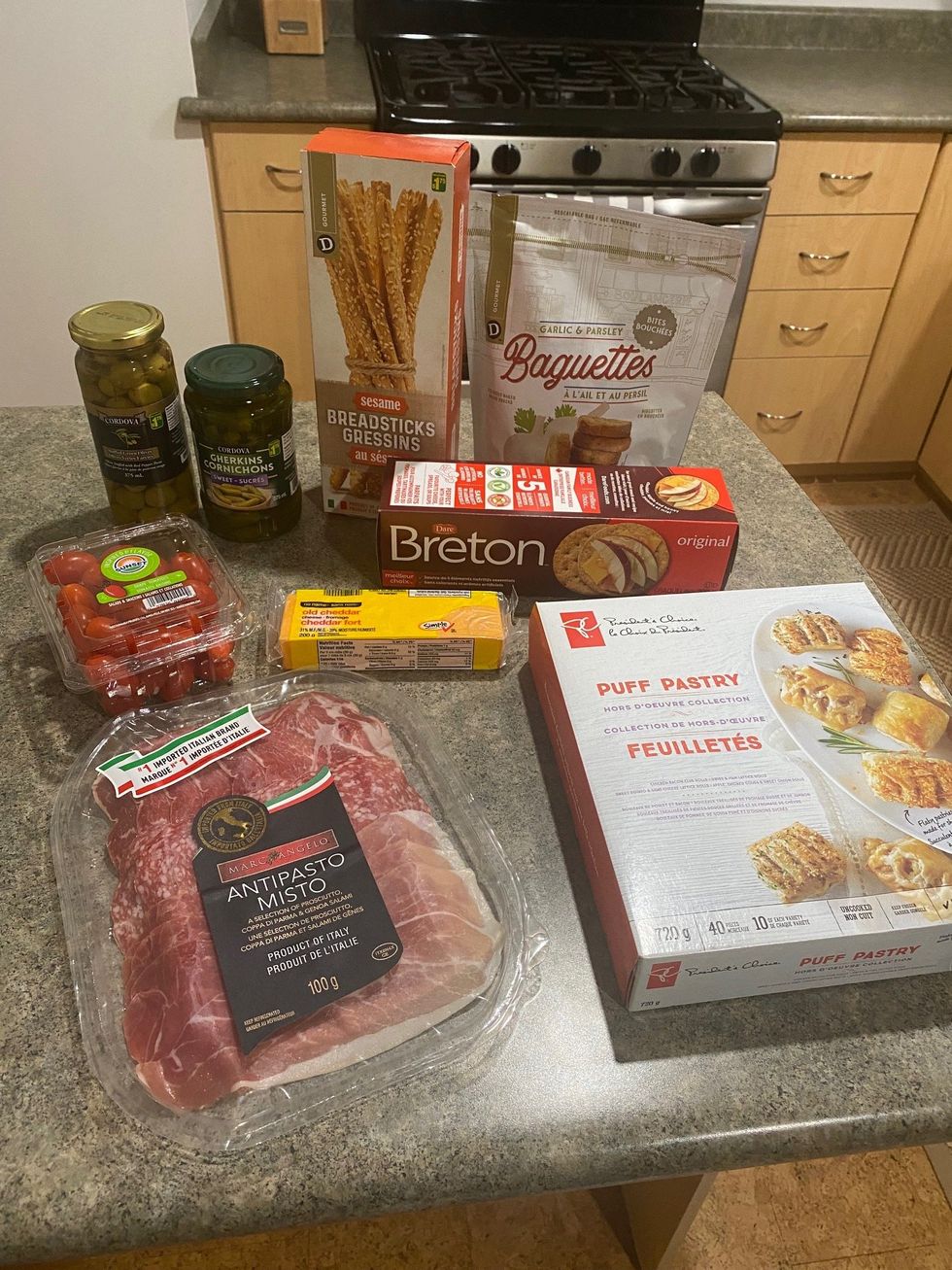 Grape tomatoes, antipasto, puff pastries, crackers, breadsticks, olives and gherkins on a kitchen counter.